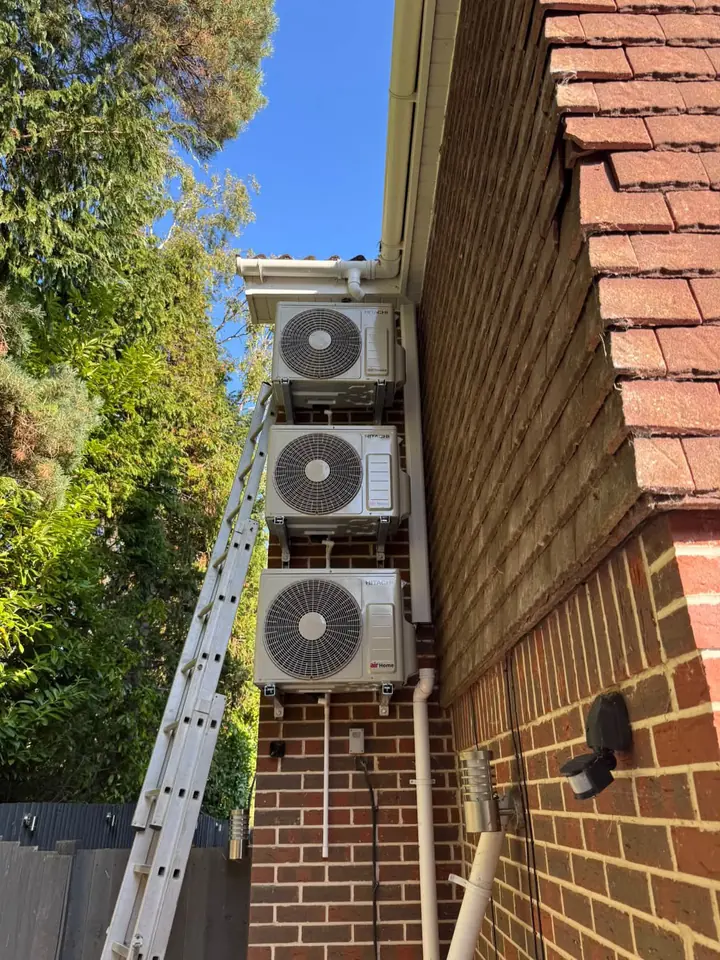 Three outdoor air conditioning units mounted vertically on a brick wall