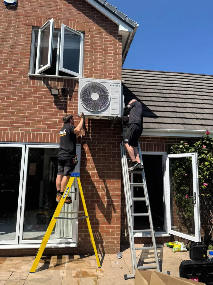 Engineers installing an outdoor air conditioning unit on a brick house